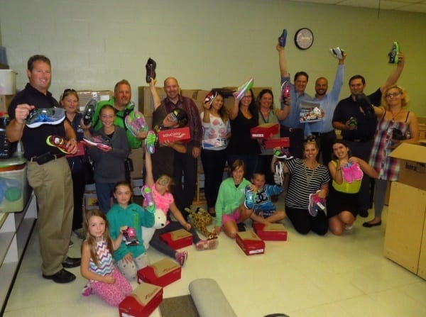 A group of Skyline employees are pictured with children holding up their new pairs of shoes