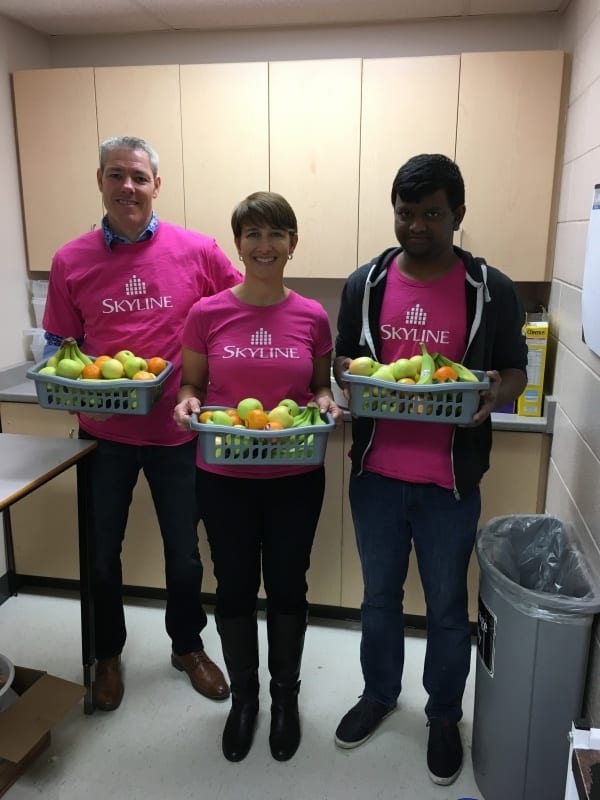 Three Skyline members hold three baskets of oranges, apples, and bananas